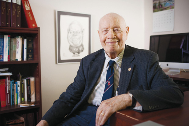 Smiling Ed Finn is sitting at his desk in a suit and a tie.