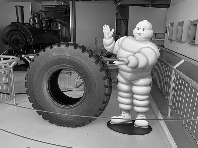 A photograph of a museum display. A large Michelin Man figure points at a large Michelin tire.
